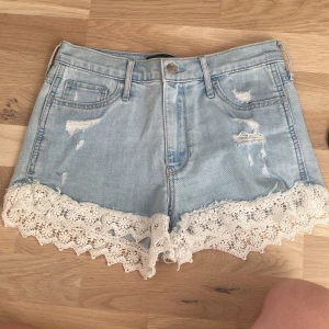 Ljusblå jeansshorts med spetskant - Supersöta ljusblå jeansshorts med slitna detaljer och vit blommig spetskant längst ner. Klassisk femficksmodell med snygga sömmar på bakfickorna. Perfekta för sommarens alla äventyr och ger en romantisk touch till din outfit.
