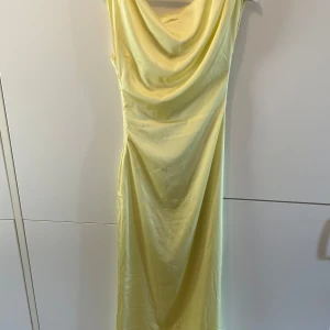 Ljusgul fest/ långklänning från Peppermayo - Supersnygg långklänning i ljusgul satin från Peppermayo. Klänningen har en draperad urringning och är ärmlös, vilket ger en elegant och trendig look. Perfekt för dig som vill sticka ut med en stilren och fräsch vibe.