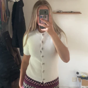 Vit kofta med kort ärm och pärlknappar - Supersöt vit kofta med korta ärmar och dekorativa pärlknappar framtill. Koftan är stickad och har en klassisk, feminin look som passar perfekt till både jeans och kjol. Enkel att styla och riktigt fräsch till våren!