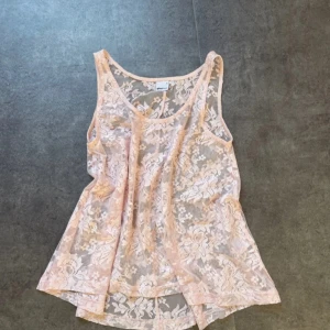 Rosa spetslinne från Gina Tricot - Säljer ett ljusrosa, ärmlöst linne från Gina Tricot i transparent spets med blommigt spets mönster. Linnet har rund halsringning och är perfekt för lager-på-lager eller som statement-piece. Linnet har en flowig look💞