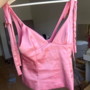 Rosa satinlinnetopp med knytband - Supersöt rosa linnetopp i satin med breda axelband som knyts på axlarna. Toppen har en figurnära passform och v-ringning framtill. Linnet är helt slutsåld från zara! prislapp kvar💕