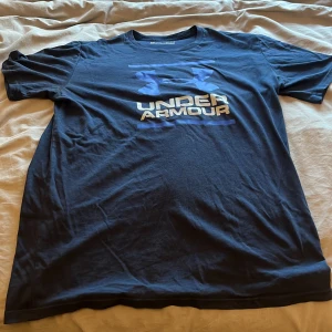 Blå Under Armour t-shirt loose fit - Snygg marinblå t-shirt från Under Armour med stort logotryck i blått och vitt på bröstet. Modellen är loose fit och har korta ärmar. Perfekt för träning eller chill dagar. Tillverkad i mjukt och lätt material som andas.