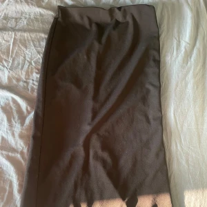 Svart långkjol med slits - En svart långkjol med stilren design och slits bak för extra rörelsefrihet. Kjolen har en rak passform och är tillverkad i ett mjukt tyg som ger en clean och klassisk look. Perfekt för dig som gillar minimalistiska vibes.