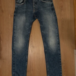 Nudie Jeans Big Bengt blå jeans 32/34 - Säljer ett par klassiska blå jeans med fade från Nudie Jeans, modell Big Bengt. Jeansen är i 100% bomull med snyggt slitna detaljer och kontrastsömmar. De har raka ben och normal passform, samt broderade bakfickor.