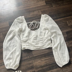 Vit croppad blus från Nelly - Superfin vit croppad blus från Nelly med långa puffärmar och snygg knytning i ryggen. Har aldrig använt och är i super bra skick, storlek 38.
