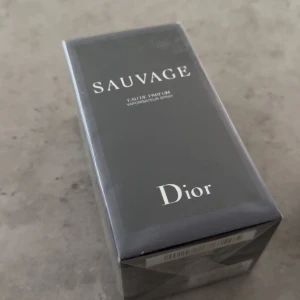 Dior Sauvage Eau de Parfum - Dior Sauvage Eau de Parfum i elegant svart kartong med silverfärgade detaljer. Parfymen kommer i en stilren, rektangulär förpackning och är känd för sin fräscha och maskulina doft. Perfekt för dig som gillar exklusiva och moderna dofter.