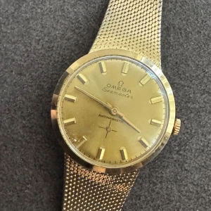 Omega Seamaster guld herrklocka - Säljer en klassisk Omega Seamaster herrklocka i guld med mesh-armband. Klockan har rund boett, stilren urtavla med guldfärgade index.Perfekt för dig som gillar vintage och exklusiv stil. GULDFÄRGAD! INTE ÄKTA 