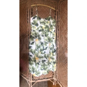 Vit sommarklänning med citronmönster H&M - Fräsch vit klänning från H&M med grönt och gult citronmönster, smala axelband och knappar framtill. Tillverkad i linnemix. Perfekt för varma dagar med sin luftiga passform och tropiska vibe.