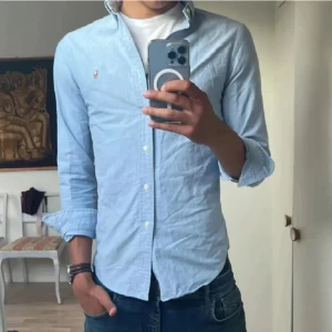 Ralph Lauren Skjorta (Pris diskuterbart) -  Säljer en klassisk ljusblå skjorta i ny skick från Ralph Lauren i SLIMFIT med button-down krage och broderad logga på bröstet. Skjortan har lång ärm, normal passform och är tillverkad i mjuk bomull. Perfekt till jeans eller chinos för en clean look. !! PRIS ÖR DISKUTERBART !!