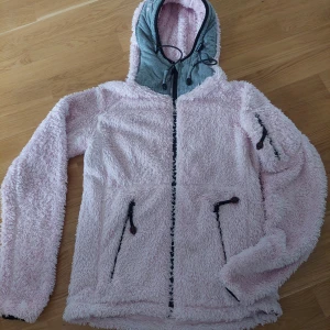 Rosa teddyjacka från Pelle P, S - Supermjuk teddyjacka i ljusrosa från Pelle P med grå huva och broderad logga. Jackan har dragkedja framtill, snörning i huvan och praktiska fickor med dragkedja. Perfekt för dig som gillar en chill och cozy stil.