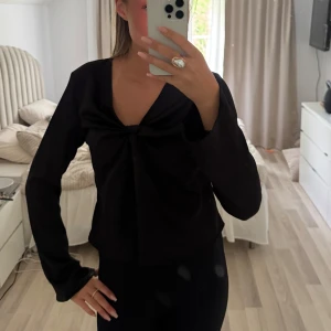 Svart långärmad topp med twistad detalj - Säljer en svart långärmad topp med v-ringning och twistad detalj framtill. Toppen har en figurnära passform och är tillverkad i ett mjukt material som känns bekvämt mot huden. Perfekt att styla med både jeans och kjol.