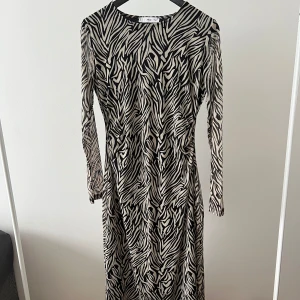 Zebramönstrad långärmad klänning från Mango - Säljer en långärmad klänning från Mango med zebramönster i svart och beige. Klänningen har rund halsringning och är figurnära i modellen. Perfekt för dig som vill sticka ut med ett djurmönstrat plagg.