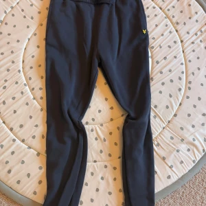 Mörkblå mjukisbyxor från Lyle & Scott Junior - Säljer ett par mörkblå mjukisbyxor från Lyle & Scott Junior med resår i midjan och det klassiska gula logobroderiet på benet. Perfekta för en avslappnad stil och riktigt sköna att ha på sig. Storlek (15-16 år) Väldigt bra skick 