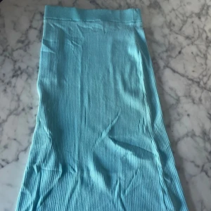 Turkos ribbad långkjol - Säljer en turkos ribbad långkjol med stretchig midja. Kjolen har en enkel och stilren design som passar perfekt till sommaren. Materialet är mjukt och följsamt, vilket gör den bekväm att bära.