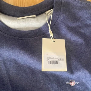 Blå sweatshirt från Gant - Mörkblå sweatshirt från Gant med rund halsringning och broderad logotyp på bröstet. Tröjan har långa ärmar och är tillverkad i mjukt material, perfekt för en avslappnad stil. Billigare vid snabb affär