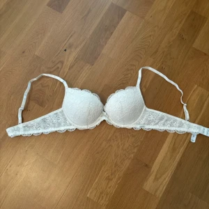 Vit push-up BH - Säljer en vit bh med spetsdetaljer och vadderade kupor. Bh:n har justerbara axelband och en liten spetskant längs nederdelen för en extra söt touch.