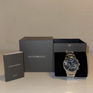 Emporio Armani herrklocka i silver - Stilren herrklocka från Emporio Armani med silverfärgad länk i rostfritt stål och svart urtavla. Klockan har flera små urtavlor och tydliga indexmarkeringar. Levereras i originalask med manual. Den här vanliga repor och en repa på glaset men annars funkar den klockrent! Ordinare pris 3999 finns även extra länkar till klockan! 