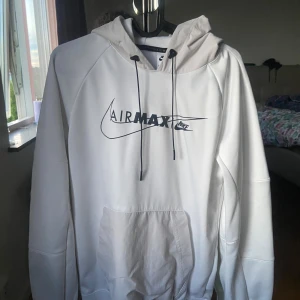 Vit hoodie Air Max från Nike - Säljer en vit hoodie från Nike Air Max med svart tryck framtill. Tröjan har huva med dragsko och en stor magficka. Perfekt för dig som gillar sportig och stilren look. FÖRST TILL KVARN!
