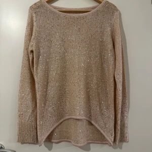 Beige stickad tröja med paljetter - Säljer en beige stickad tröja med glittriga paljetter över hela plagget. Tröjan har lång ärm, rund halsringning och en något längre bakdel. Perfekt för dig som vill ha lite extra glitter i vardagen.