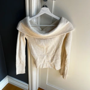 Offshoulder ribbad tröja från H&M - Säljer en krämvit ribbad offshoulder-tröja från H&M i storlek XS. Tröjan har långa ärmar och en bred, nedvikt krage som ger en snygg och trendig look. Perfekt att styla med jeans eller kjol.