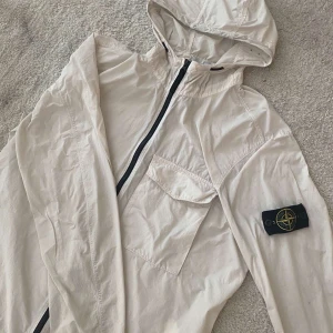 Vit vindjacka från Stone Island - Säljer min stilrena vita Stone Island jacka i storlek L men passar även M. Jackan är i fint skick och perfekt för våren/sommaren. Har originalbadge på ärmen och kvitto finns som bevis på äkthet. Obs! Ett litet hål på axeln bild på hålet får ni privat, men inget som påverkar funktionen eller looken. Säljes p.g.a. rensning.  💸 Pris kan diskuteras vid snabb affär! 