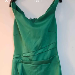 Grön volangklänning med v-ringning - Snygg grön klänning med v-ringad hals och volangdetaljer nertill. Klänningen har en figurnära passform och asymmetrisk nederkant som ger en cool look. Perfekt för dig som vill sticka ut med färg och form.