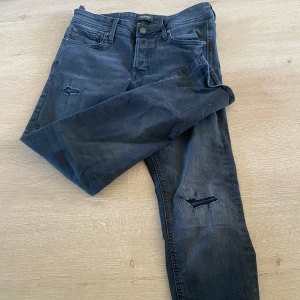 Jeans slim fit - Säljer ett par svarta jeans med snygga slitningar på båda benen. Klassisk femficksmodell med knapp och dragkedja i gylfen. Jeansen har en rak passform och är perfekta för en avslappnad stil. Använda 1 gång, jag e 175 å dem sitter perfekt. Jack and jones 