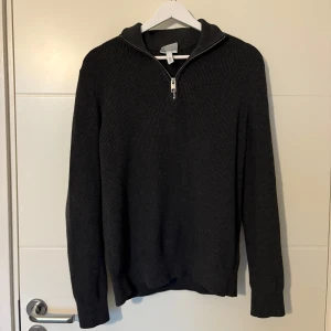 Mörkgrå stickad tröja med dragkedja - Mörkgrå stickad tröja med halv dragkedja vid halsen. Slim fit-modell med långa ärmar. Perfekt för lager-på-lager och enkel att matcha med ett par snygga jeans eller andra outfits!