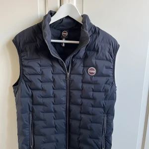 Svart dunväst från Colmar - Snygg svart dunväst från Colmar med hög krage och dragkedja framtill. Västen har två fickor med dragkedja och Colmar-logga på bröstet. Perfekt för lager-på-lager och enkel att matcha.