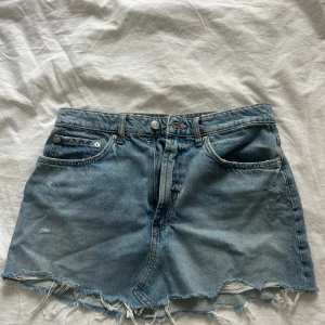 Blå jeanskjol med sliten snygg kant - Säljer en klassisk blå jeanskjol med rå, fransig nederkant och femficksmodell. Kjolen har normal passform och är i kort längd, perfekt till sommaren. Stängs med knapp och dragkedja framtill. Enkel och tidlös design. Aldring använd, men tog av prislappen så kunde ej lämna tillbaka den. Stolek L, men väldigt liten i storleken, passar mig som brukar ha S/M💓