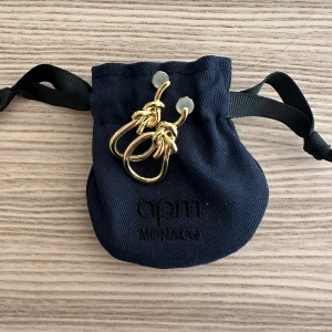 Guldiga örhängen från APM Monaco - Säljer ett par snygga guldiga örhängen från APM Monaco. De har en unik design med dubbla ringar och knutdetalj. Perfekta för att lyfta din stil! Levereras i originalpåse.