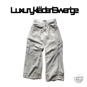 Japansk jeans fr ItAms Studio - Säljer ett par beige cargopants från ItAms Studio med bred passform och flera fickor på sidorna. Byxorna har dragkedja och knapp framtill samt tydliga sömdetaljer längs benen. Perfekta för en avslappnad och trendig stil.