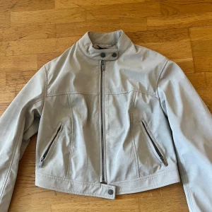 Beige kort skinn/mocka jacka - Säljer en snygg beige kort skinn/mocka jacka från Gina tricot. Jackan har dekorativa knappar vid halsen och längst ner. Snygg och stilren modell som passar till mycket. Har använt den typ 2 gånger men känner inte att den passar mig. Nypris 799. Skriv vid funderignar🥰