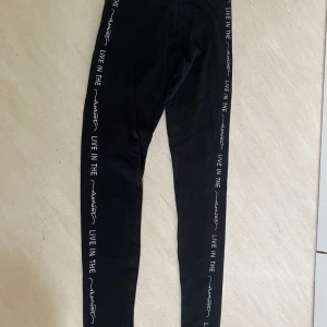 Svarta leggings från Esmara med text - Svarta leggings från Esmara med vit text längs benen. Tillverkade i bomull och elastan för en bekväm och stretchig passform. Perfekta för en avslappnad stil eller till träning.