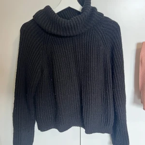 Svart stickad polotröja - Mysig svart stickad polotröja med grov ribbad struktur och hög polokrage. Perfekt för kyliga dagar och enkel att styla till olika outfits. Tröjan har lång ärm och avslappnad passform.