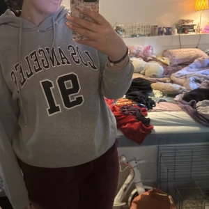 Grå hoodie med tryck från SHEIN - Grå hoodie från SHEIN med svart och vitt tryck 'LOS ANGELES 91' på framsidan. Klassisk huva med dragsko och normal passform. Perfekt för en avslappnad stil.