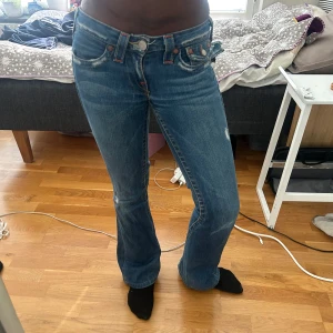 Blå bootcut jeans från True Religion -  klassiska blå jeans från True Religion med bootcut-passform och snygga detaljer på bakfickorna. Jeansen har låg midja.