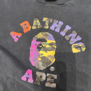 Svart t-shirt från A Bathing Ape som är RARE - Säljer en svart t-shirt från A Bathing Ape med ikoniskt färgglatt camo-tryck och logga på bröstet. Klassisk rund hals och korta ärmar. Perfekt för dig som gillar streetwear och vill sticka ut med en unik design.