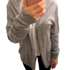 Ljusgrå kofta från Scotch & Soda - Säljer en stilren ljusgrå kofta från Scotch & Soda. Koftan är öppen framtill, har långa ärmar och är tillverkad i ett mjukt, tunt material. Perfekt att slänga över en skjorta eller t-shirt för en avslappnad look.