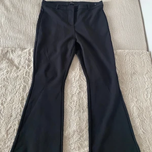 Svarta bootcut kostymbyxor från Vero Moda - Snygga svarta kostymbyxor från Vero Moda med bootcut-passform. Byxorna har hög midja och klassisk design med bälteshällor och diskret stängning framtill. Perfekta för en stilren look.