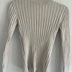Beige ribbad långärmad tröja - Säljer en beige ribbad långärmad tröja med rund hals. Tröjan har en tight passform och är perfekt att styla till olika outfits. Enkel och stilren design som passar året runt.