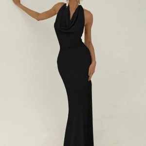 Svart långklänning med halterneck - Säljer en elegant svart långklänning med draperad halsringning och öppen rygg. Klänningen har en tight passform och är ärmlös, perfekt för festliga tillfällen. Materialet är mjukt och följsamt för en snygg siluett. Helt oanvänd i storlek XS. 