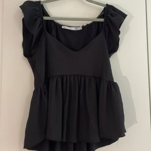 Volangtopp - Säljer en svart topp med volangdetaljer och v-ringning. Perfekt till både vardags och fest