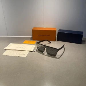 Svarta LV glasögon  - Snygga svarta solglasögon från Louis Vuitton med LV-monogram på glasen. Raka, mattsvarta bågar i plast och stora, kantiga linser. Kommer med originalfodral, putsduk och ask.
