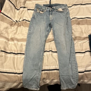 Ljusblå jeansbyxor från H&M - Ljusblå jeansbyxor från H&M med regular fit och klassisk femficksdesign. Byxorna har normal passform, knapp och dragkedja i gylfen samt en mörkblå snörning i midjan. Perfekta för en avslappnad stil.