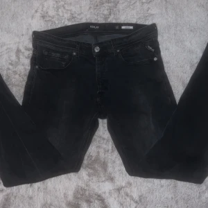 Svarta Replay Grover jeans - Säljer ett par svarta Replay Grover jeans med klassisk femficksdesign och snygga detaljer på bakfickorna. Jeansen har normal passform och är perfekta för dig som gillar stilrena och bekväma byxor. Märkeslogga på fickan och knapp. 
