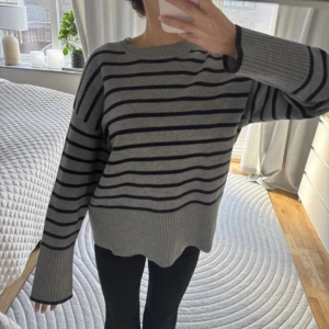  randig stickad tröja - Säljer en grå stickad tröja med marinblå horisontella ränder. Tröjan har lång ärm, rund halsringning och en något oversized passform. Ribbstickade muddar vid ärmslut och nederkant. Perfekt för kyliga dagar!