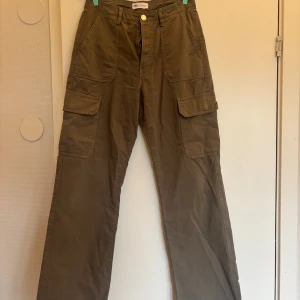 Khakigröna cargobyxor från Zara - Säljer ett par khakigröna cargobyxor från Zara med raka ben och stora fickor på sidorna. Byxorna har hög midja och stängs med knapp och dragkedja. Perfekta för en avslappnad och trendig look.