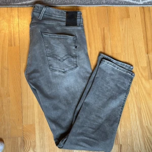 Grå jeansbyxor från Replay Anbass - Säljer ett par grå jeansbyxor från Replay, modell Anbass. Byxorna har klassisk femficksdesign, svarta detaljer och en snygg tvättad finish. Perfekta för dig som gillar stilrena och bekväma jeans med modern passform.