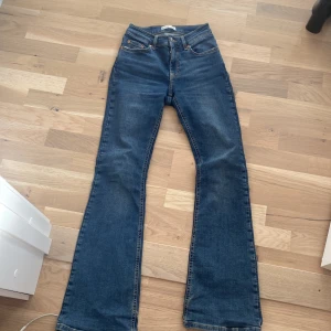 Blå bootcut jeans från ginatricot - Säljer ett par klassiska blå bootcut jeans från Levi's med fem fickor och orange sömmar. Jeansen har hög midja och en snygg utsvängd passform nertill. Perfekta för dig som gillar en tidlös denimlook.